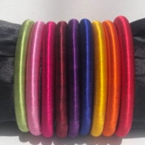 Puede incluir: Conjunto de diez pulseras de seda de colores, en tonos de verde, rosa, rojo, burdeos, morado, azul, amarillo y naranja.