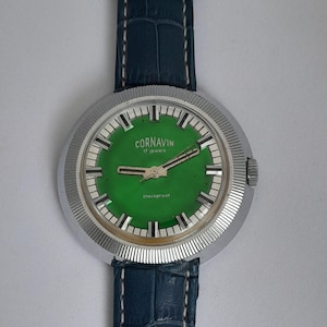 May include: A vintage Cornavin wristwatch with a green face and silver bezel. The watch has a blue leather band. The watch face displays the brand name and the words "17 jewels" and "shockproof".