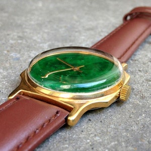 May include: A gold wristwatch with a green jade face and a brown leather band.
