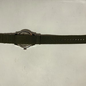 May include: A silver watch with a green nylon strap. The watch face is visible, but the time is not displayed.