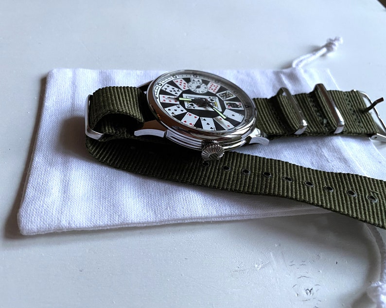 May include: A silver watch with a white face and a green nylon strap. The watch face features a design of playing cards.