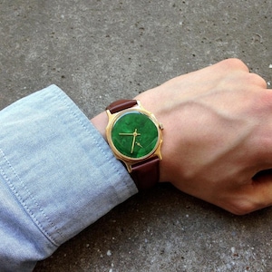 May include: A gold-tone wristwatch with a green face and brown leather band.