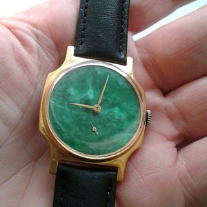 May include: A gold-tone wristwatch with a green, marbled face and black leather band.