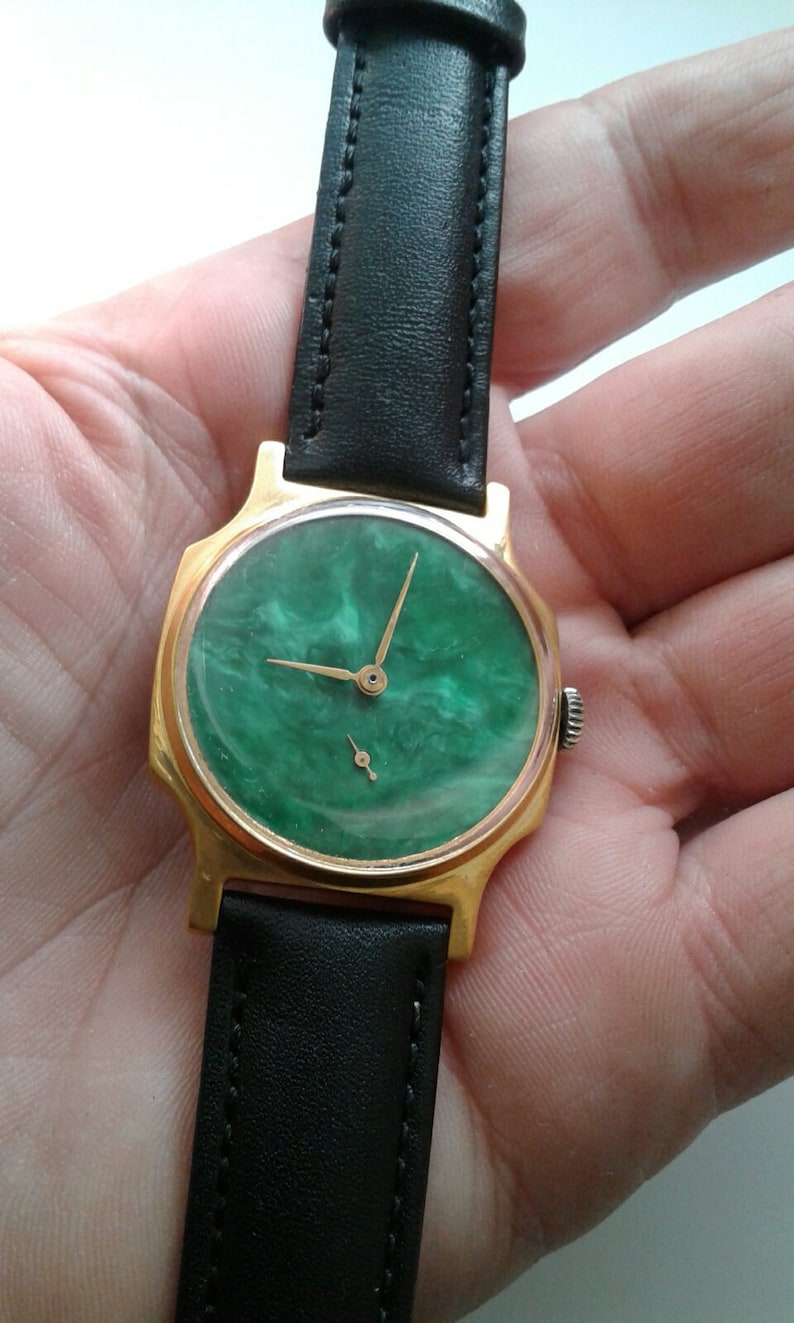 May include: A gold-tone wristwatch with a green, marbled face and black leather band.