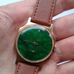 May include: A gold-tone wristwatch with a green face and brown leather band.