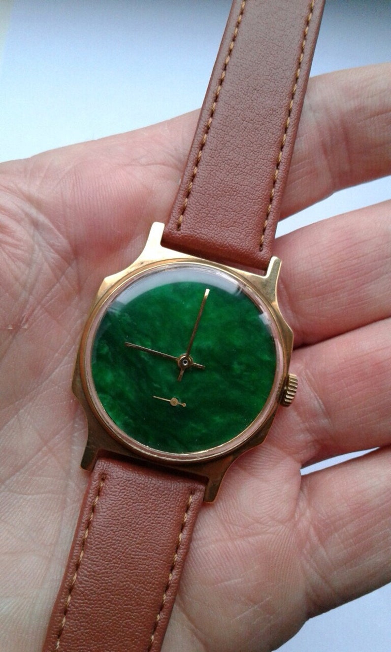 May include: A gold-tone wristwatch with a green face and brown leather band.