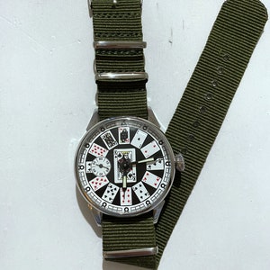 May include: A silver wristwatch with a green nylon strap. The watch face features a unique design with playing cards instead of numbers.