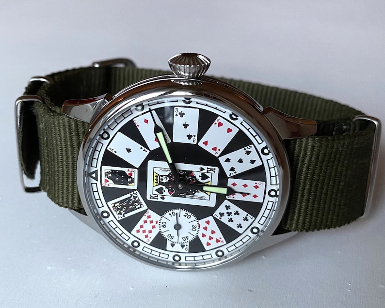 May include: A silver wristwatch with a black face and playing card design. The watch has a green nylon strap.