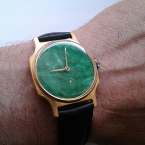 May include: A gold-tone wristwatch with a green marbled face and black leather band.