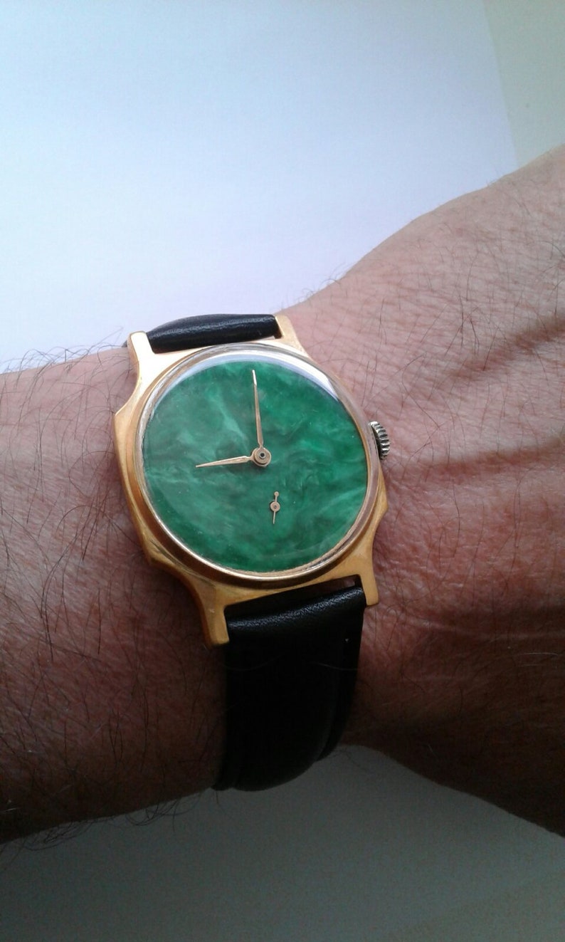 May include: A gold-tone wristwatch with a green marbled face and black leather band.