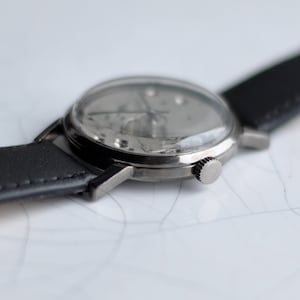 May include: A silver wristwatch with a black leather band. The watch face is silver and has black hands and markers.