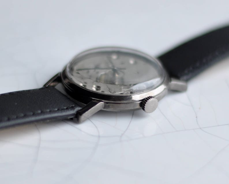 May include: A silver wristwatch with a black leather band. The watch face is silver and has black hands and markers.