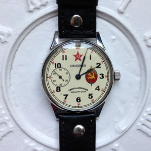 May include: A vintage wristwatch with a white face and black hands. The watch face has red accents and the text "КОМАНДИРСКИЕ" and "СМЕРТЬ ШПИОНАМ ЗАКАЗ ГРУ СССР".