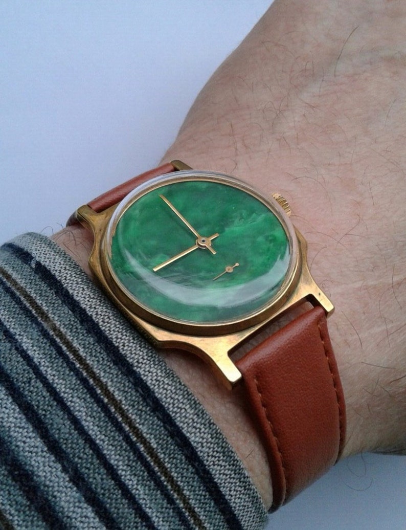 May include: A gold-tone wristwatch with a green face and a brown leather band.