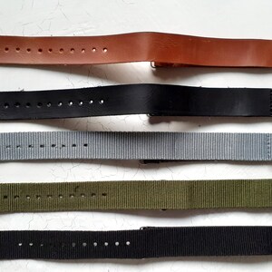 Puede incluir: Una selecci&oacute;n de correas de reloj en varios colores. Las correas incluyen cuero marr&oacute;n, cuero negro, nailon gris, nailon verde oliva y nailon negro. Cada correa tiene una hebilla plateada y est&aacute; dise&ntilde;ada para un reloj.