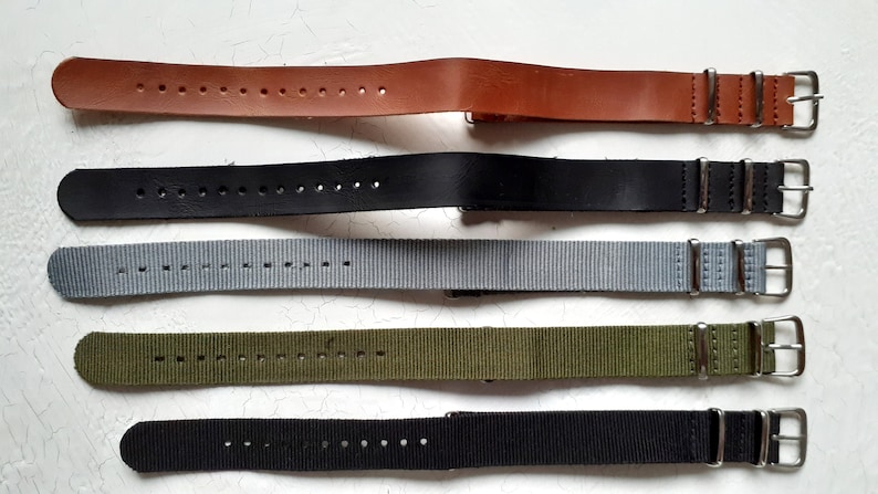 Puede incluir: Una selecci&oacute;n de correas de reloj en varios colores. Las correas incluyen cuero marr&oacute;n, cuero negro, nailon gris, nailon verde oliva y nailon negro. Cada correa tiene una hebilla plateada y est&aacute; dise&ntilde;ada para un reloj.