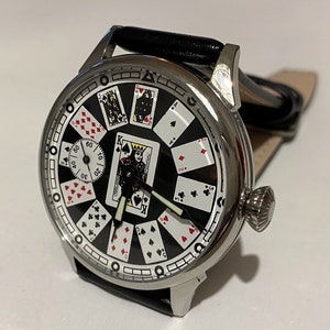 May include: A silver pocket watch with a black face and playing card design. The watch has a black leather band and a silver crown.