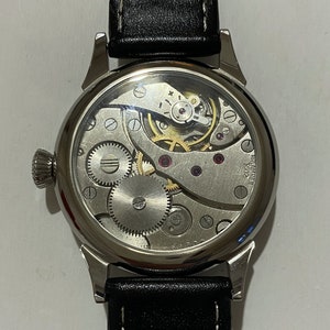 May include: A silver wristwatch with a black leather band. The watch face is clear and shows the inner workings of the watch.