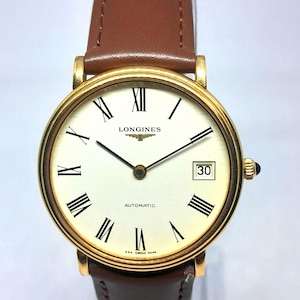 May include: A gold-toned Longines automatic wristwatch with a cream-colored face, black Roman numerals, and a date display at the 3 o'clock position. The watch has a brown leather strap.