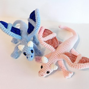 May include: Two crocheted dragon toys, one light blue with blue wings and one pink with brown wings.