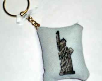 May include: A small blue fabric keychain with a black embroidered image of the Statue of Liberty. The keychain has a gold metal ring and chain.