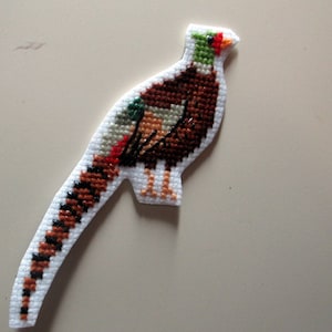 May include: A cross-stitch of a brown and white pheasant with a long tail. The pheasant is standing on a white background.