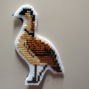 Puede incluir: Un adorno de pájaro de punto de cruz marrón y blanco con cabeza y pico negros.