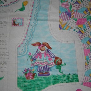 May include: A blue and white fabric panel with a bunny holding a basket of flowers. The bunny is wearing a pink and white dress with purple stripes. The fabric panel is part of a quilting pattern called "Springtime Vest" by LaLynne Designs.