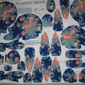 May include: A fabric pattern sheet with instructions for making a plush toy rabbit. The pattern pieces are printed on a white background with a blue floral design. The title of the pattern is "Ravishing Rabbits".