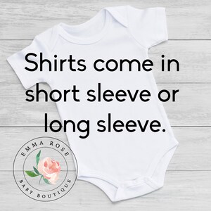 May include: White baby onesie with the text "Shirts come in short sleeve or long sleeve." The onesie has a round neckline and short sleeves. The Emma Rose Baby Boutique logo is at the bottom.