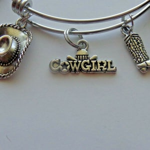 May include: A silver charm bracelet with multiple charms, including a cowboy hat, a boot, and a charm that says "COWGIRL".