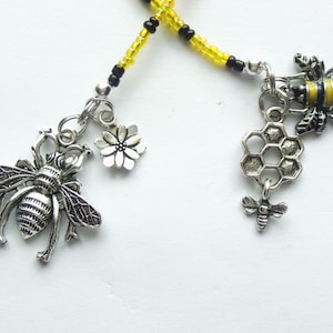 May include: A beaded necklace with bee and honeycomb charms. The necklace is made with black and yellow beads. The charms are silver and feature a bee, a honeycomb, and a flower.