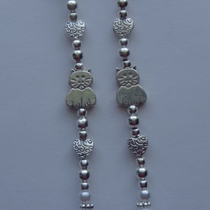 May include: Two silver chains with alternating silver beads, heart charms, and cat charms.
