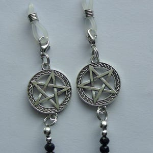 May include: A pair of silver-toned nipple clamps featuring a circular pentagram charm with a braided border design. Each charm is attached to a clear silicone loop with a metal spring mechanism and a small silver bead accent above a black beaded chain.