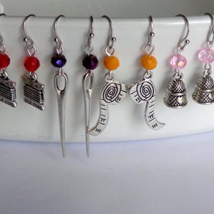 May include: A collection of handmade earrings with silver-tone charms and colorful beads. The charms include spools of thread, needles, measuring tapes, and thimbles. The earrings are displayed against a white background.