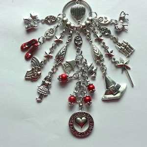 May include: A silver-toned keychain with charms featuring elements from The Wizard of Oz. Charms include ruby slippers, a witch's hat, a star wand, and a heart-shaped pendant with the words "Home There's No Place Like Home."