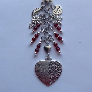 May include: A silver-toned keychain with various charms, including a heart pendant with the words "Mother and Daughter forever." It features red beads, a heart-shaped charm with "I love you," and leaf and flower charms.