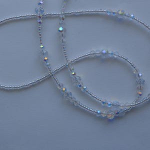 May include: A white beaded necklace with iridescent crystal accents. The necklace is made of small, round beads and features larger, faceted crystals that add sparkle and dimension.