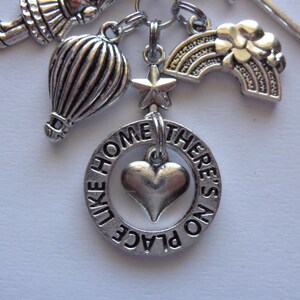 May include: Silver-toned charm bracelet with various charms, including a hot air balloon, a rainbow, a star, and a heart within a ring that reads "LIKE HOME THERE'S NO PLACE". The charms are connected by small metal rings.