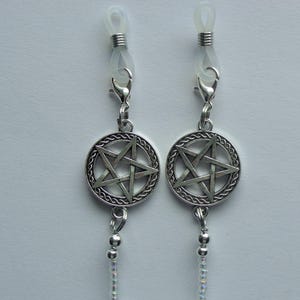May include: A pair of silver-toned eyeglass chains featuring circular pentagram charms with intricate braided borders. Each chain attaches to glasses with clear silicone loops and silver metal coils, connected by lobster claw clasps.