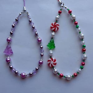 May include: Two beaded Christmas-themed charms. One features purple beads and a purple tree charm. The other has red, green, and white beads with candy cane and Christmas tree charms. Both have a silver-colored clasp.