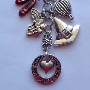 May include: A silver charm bracelet with multiple charms, including red shoes, a rainbow, a hot air balloon, a witch's hat, and a heart-shaped pendant with the words "LIKE HOME THERE'S NO PLACE".