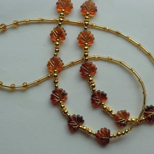 May include: A necklace featuring a delicate design with amber-colored leaf-shaped beads and small gold-colored beads. The necklace has a double strand design, with the leaf beads evenly spaced along the strands.