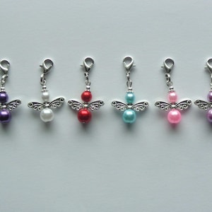 May include: Six silver-toned metal angel charms with lobster claw clasps. Each charm features a pair of decorative filigree wings and two round beads in purple, white, red, turquoise, light pink, and lavender colors arranged vertically.
