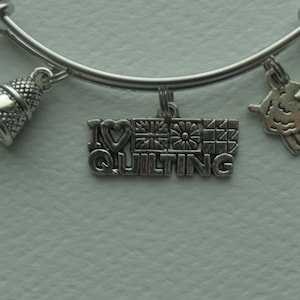May include: Silver charm bracelet with multiple charms, including a thimble, a sheep, and a charm that says "I love quilting" with a patchwork quilt design.
