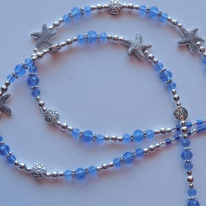 May include: A necklace featuring blue crystal beads and silver-toned accents. The necklace includes starfish charms and decorative silver beads. The design is reminiscent of the ocean and beach themes.