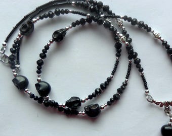 May include: A beaded necklace featuring black skull-shaped beads, faceted black glass beads, and small silver-toned metallic spacer beads. The necklace includes a silver-toned metal filigree connector piece and a single black skull bead pendant.