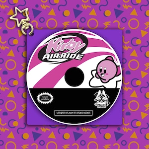 May include: A pink and white CD-shaped keychain with the text "Kirby Air Ride" and a cartoon image of Kirby. The keychain is designed by Anubis Studios and is a fan-made item, not official.