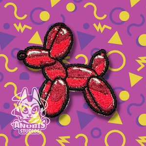 May include: Red embroidered patch of a balloon animal shaped like a dog. The patch is on a purple background with yellow and blue geometric shapes.