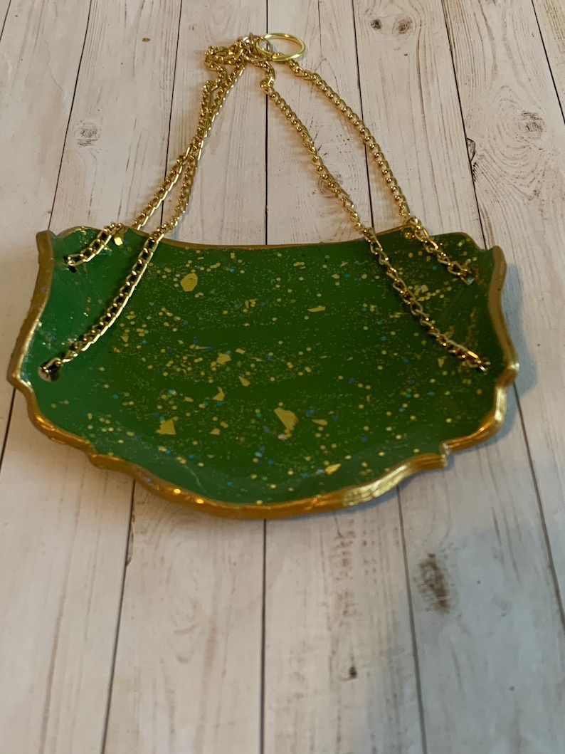 K&ouml;nnte beinhalten: Ein gr&uuml;nes und goldenes Dekotablett mit einer goldenen Kette zum Aufh&auml;ngen. Das Tablett hat eine gesprenkelte gr&uuml;ne Oberfl&auml;che mit goldenen Flocken.